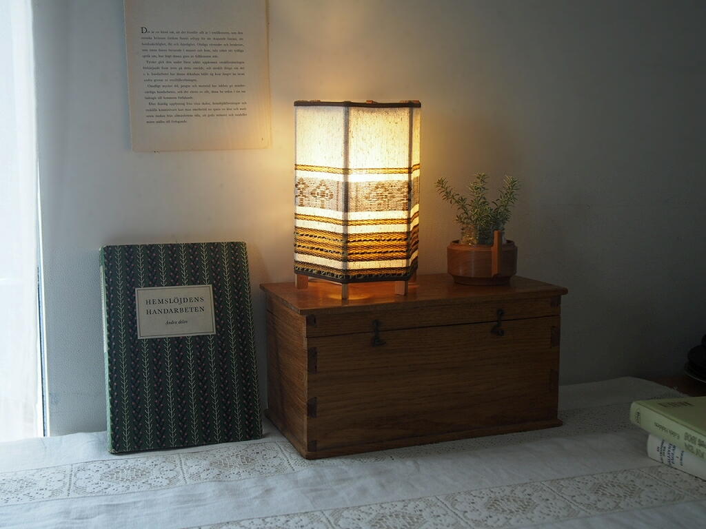 木製ボックスの上で灯りをともした北欧ヴィンテージランプ。リネンの織り模様がやわらかく浮かぶ様子。 antenna