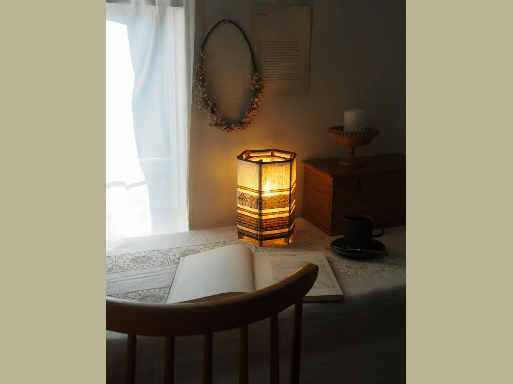 リネン刺しゅうシェードと木製ベースの六角形テーブルランプ。スウェーデン製のやさしい灯りを写した写真。 antenna