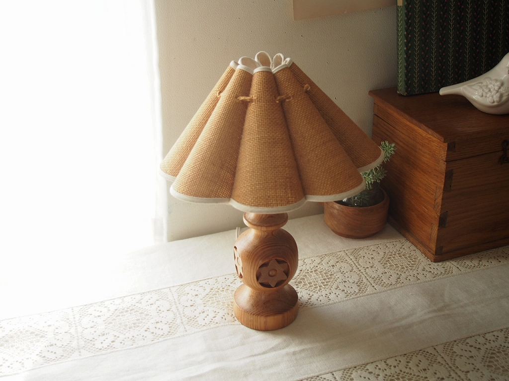 レースクロスと木箱のそばに置かれた木製ベースとジュートシェードのテーブルランプ。 antenna