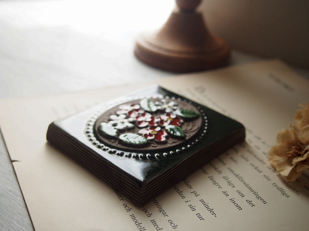 陶板を本の上に置いたスタイリング写真（釉薬の艶と色合い）。 antenna